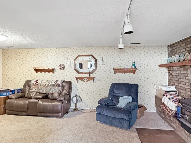 Carpeted living area featuring a brick fireplace with a wood mantel, a textured ceiling, and track lighting