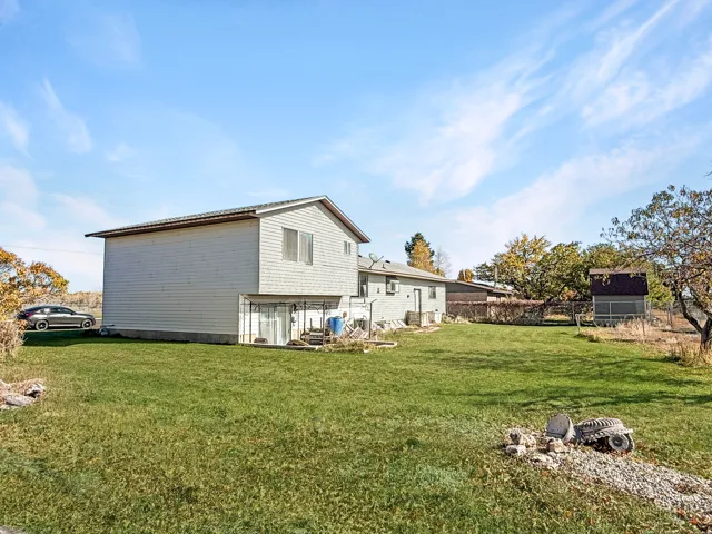 Spacious rear yard with a verdant lawn, featuring a detached outbuilding with a dark shingle roof and a fenced perimeter