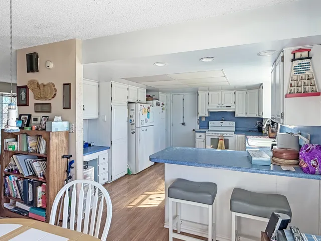 Spacious kitchen featuring white cabinetry, blue countertops, white appliances, wood-finish flooring, and recessed lighting