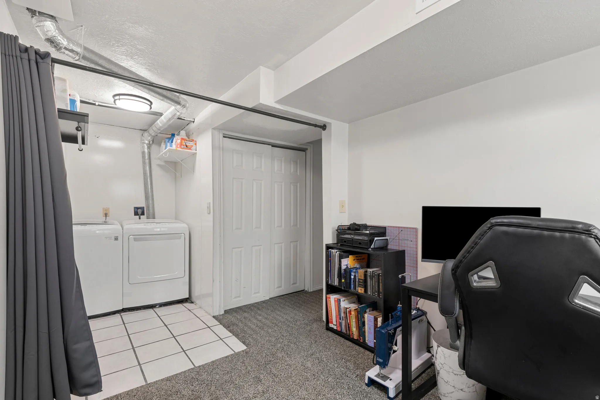 Dedicated laundry area featuring a tile floor and overhead lighting, with white bi-fold closet doors