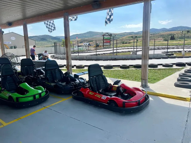 Covered outdoor staging area featuring multiple go-karts, a paved track bordered by tires, and distant mountainous terrain