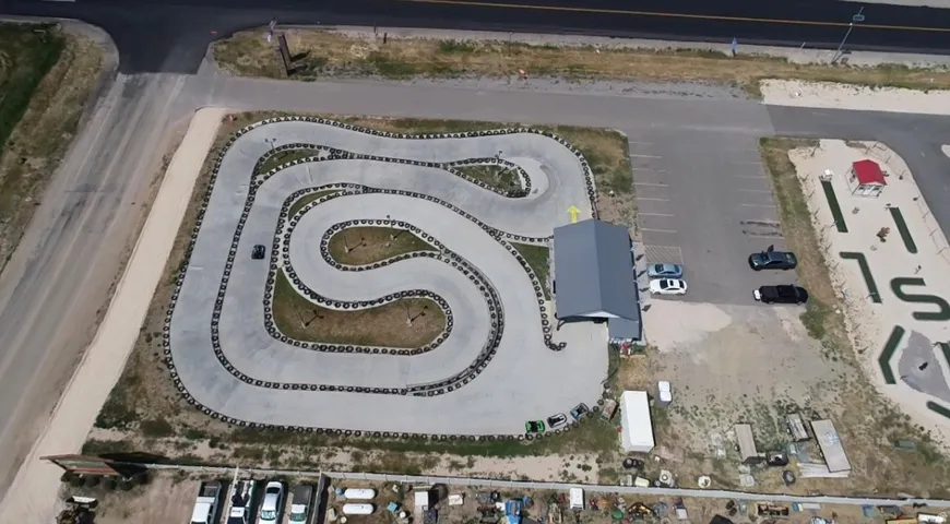 Aerial view showcasing a comprehensive entertainment property featuring a paved go-kart track with tire barriers, a building with a gray metal roof, a paved parking lot, and a distinct miniature golf course
