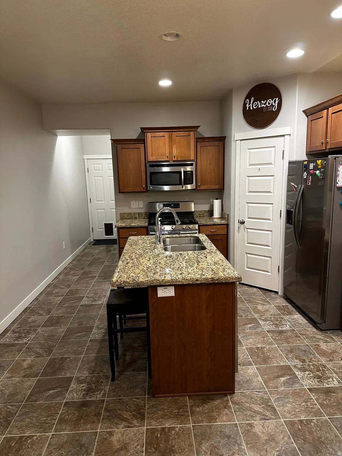 Kitchen featuring an island with a double basin sink, granite-style countertop, and recessed lighting