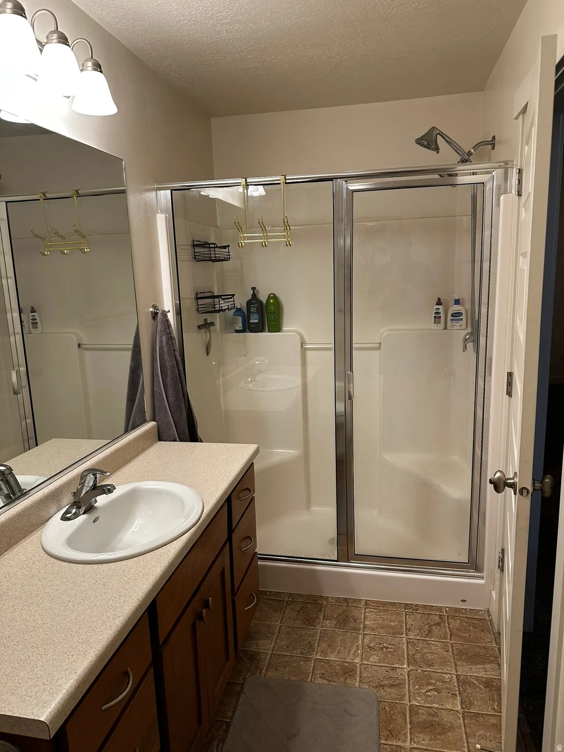 Full bathroom featuring a shower with sliding glass doors, a vanity with a drop-in sink and a light-toned countertop, wood-finish cabinetry, and tiled flooring
