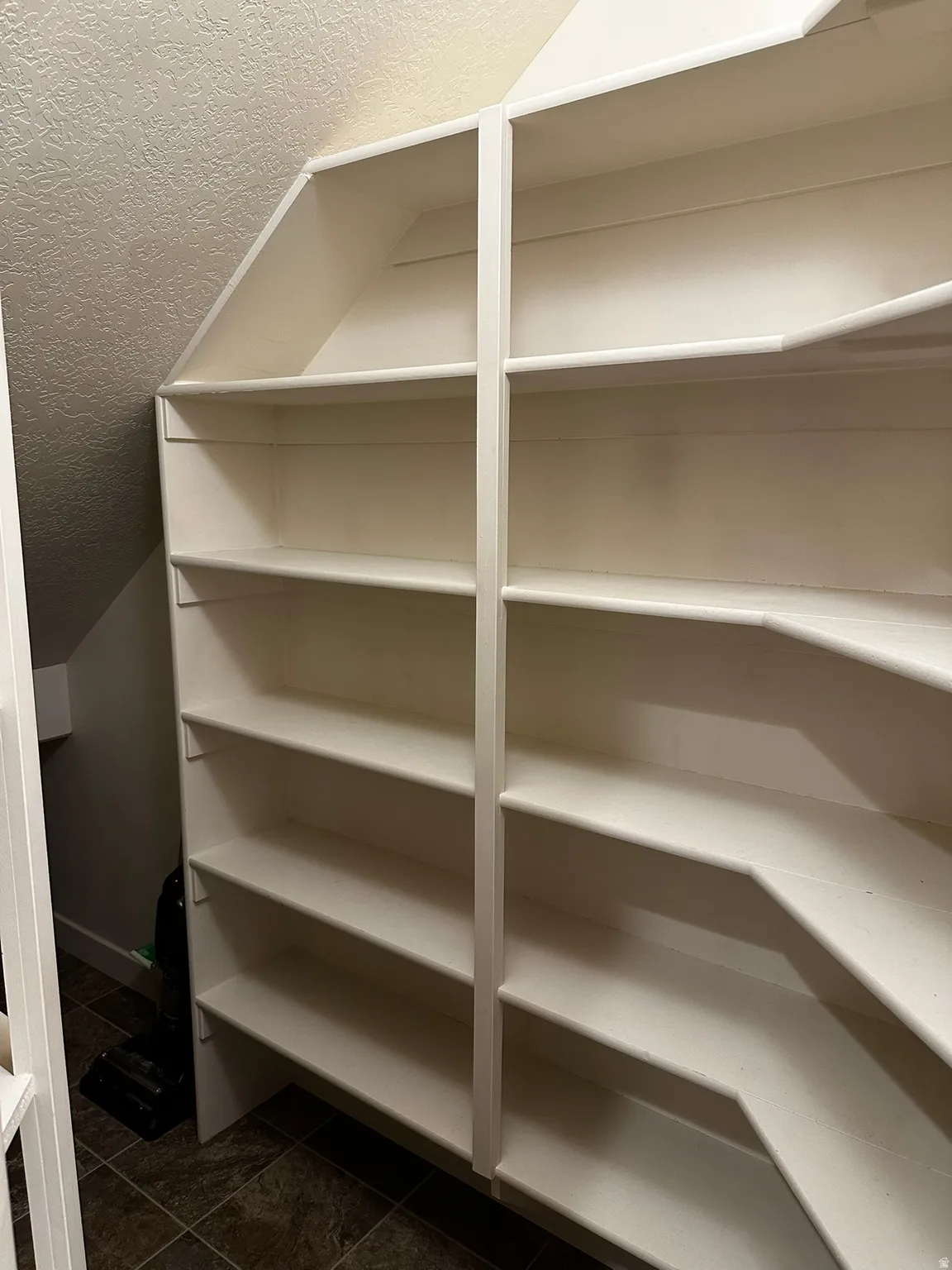 Custom built-in shelving with multiple levels, white finish, and a corner design, set against textured walls and wood-finish flooring