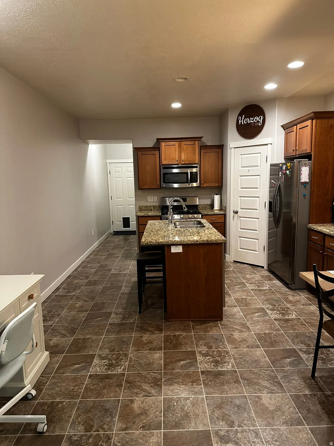 Kitchen featuring a central island with an undermount sink, stainless steel appliances, wood cabinetry, and a patterned tile floor