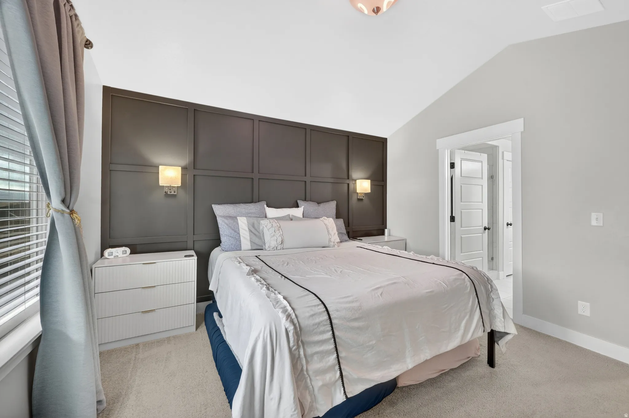 Bedroom featuring a dark paneled accent wall, vaulted ceiling, and light-colored carpet flooring