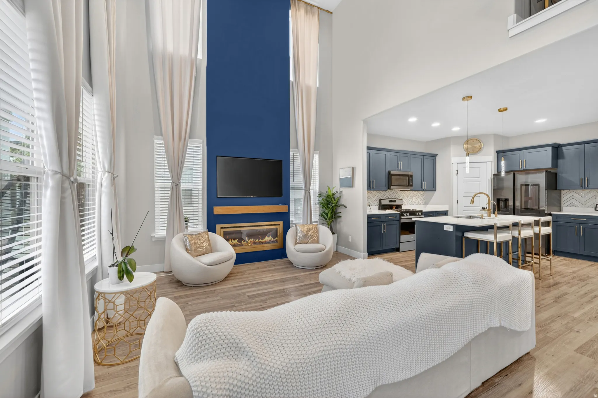 Open-concept living area featuring high ceilings, wood-finish flooring, and an electric fireplace with a wood mantle