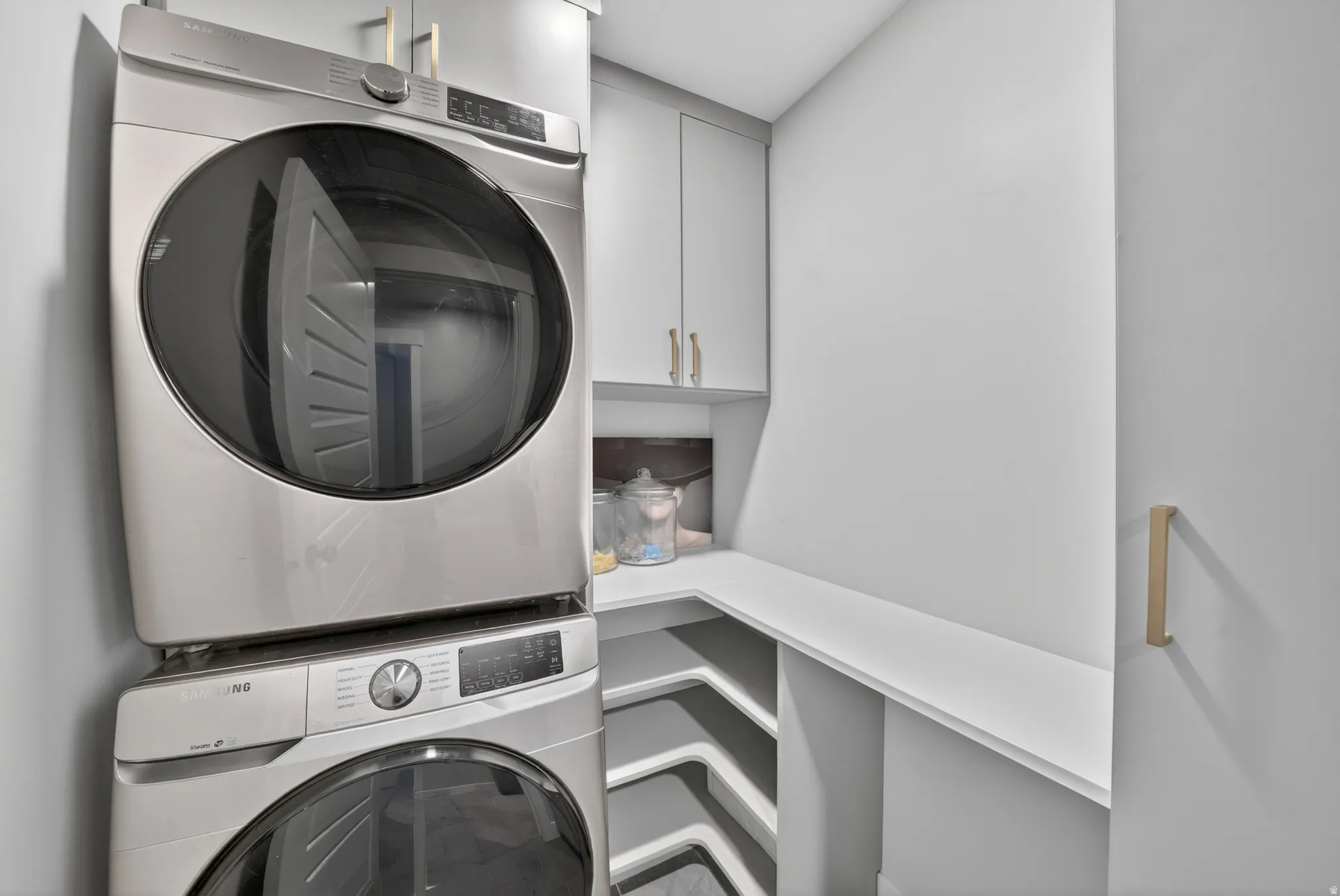 Integrated laundry appliances featuring a stacked washer and dryer, complemented by built-in upper cabinetry and a corner countertop with open shelving below