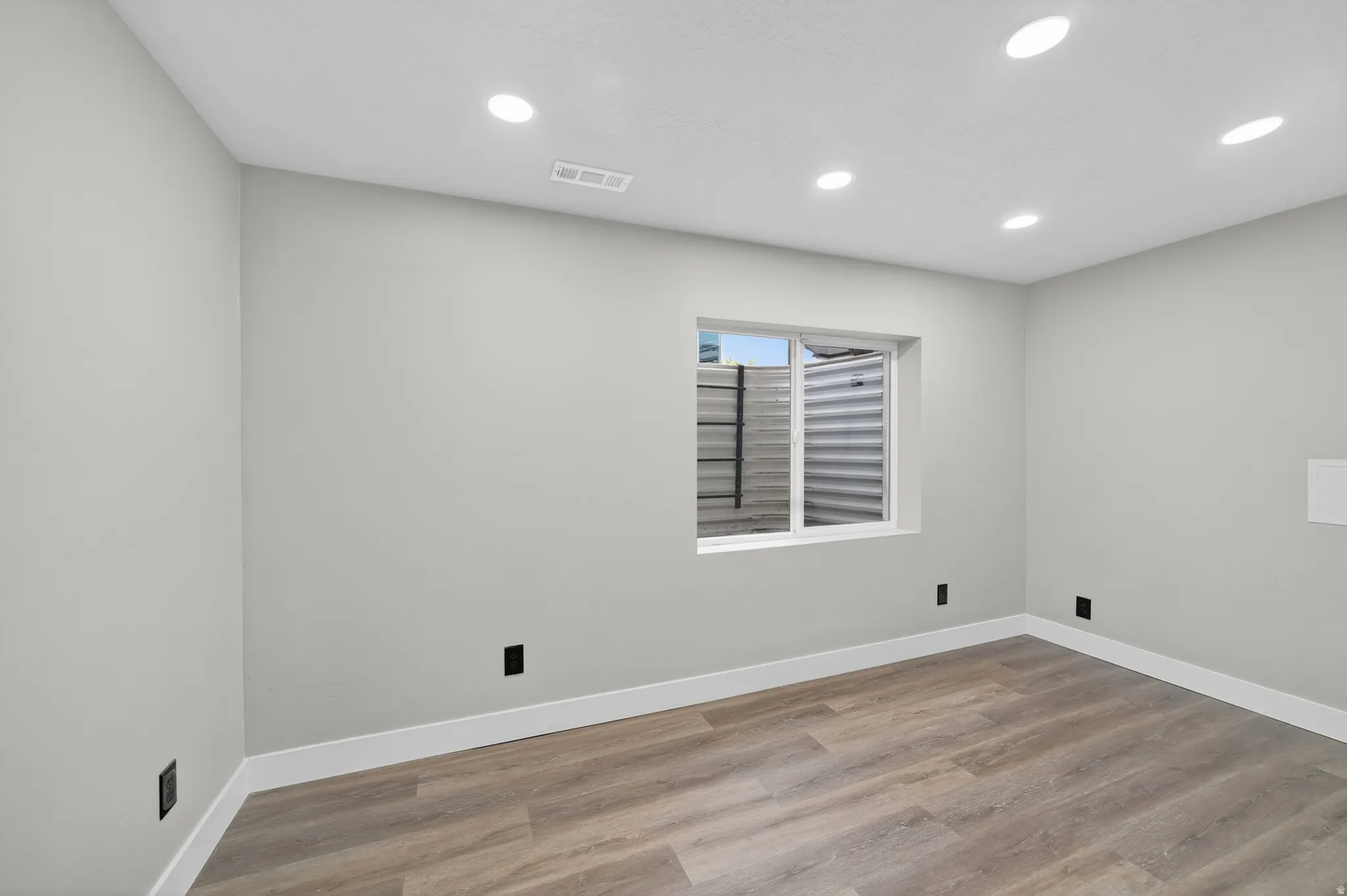 Room featuring wood-finish flooring, recessed lighting, and a window with a metal window well