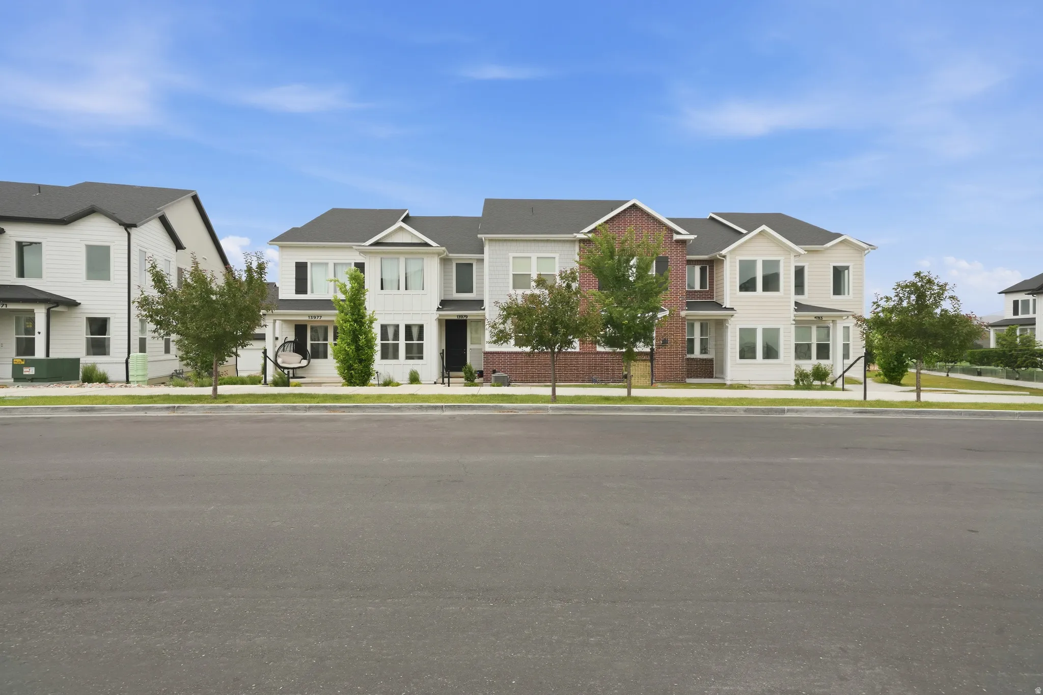 Contemporary multi-story facade featuring mixed siding, prominent gables, dark-framed windows, and a landscaped sidewalk area