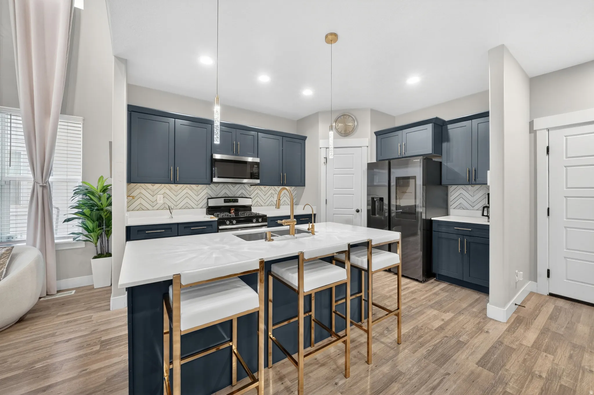 Modern kitchen featuring a large central island with seating, dark blue cabinetry, stainless steel appliances, and wood-finish flooring
