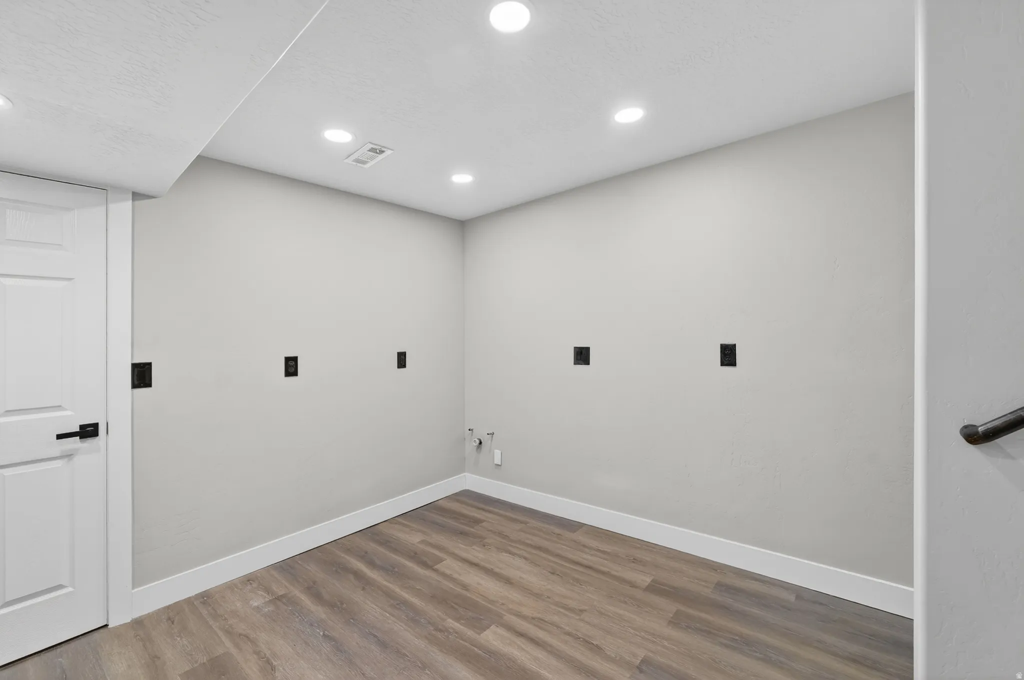 Dedicated utility space featuring wood-finish flooring, recessed lighting, a white paneled door, and a black handrail