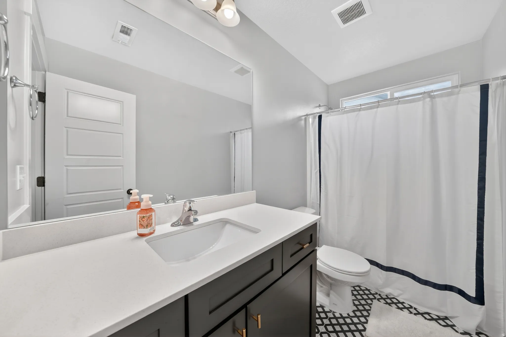Bathroom with a modern vanity featuring a white countertop, undermount sink, and dark cabinetry with gold-tone hardware