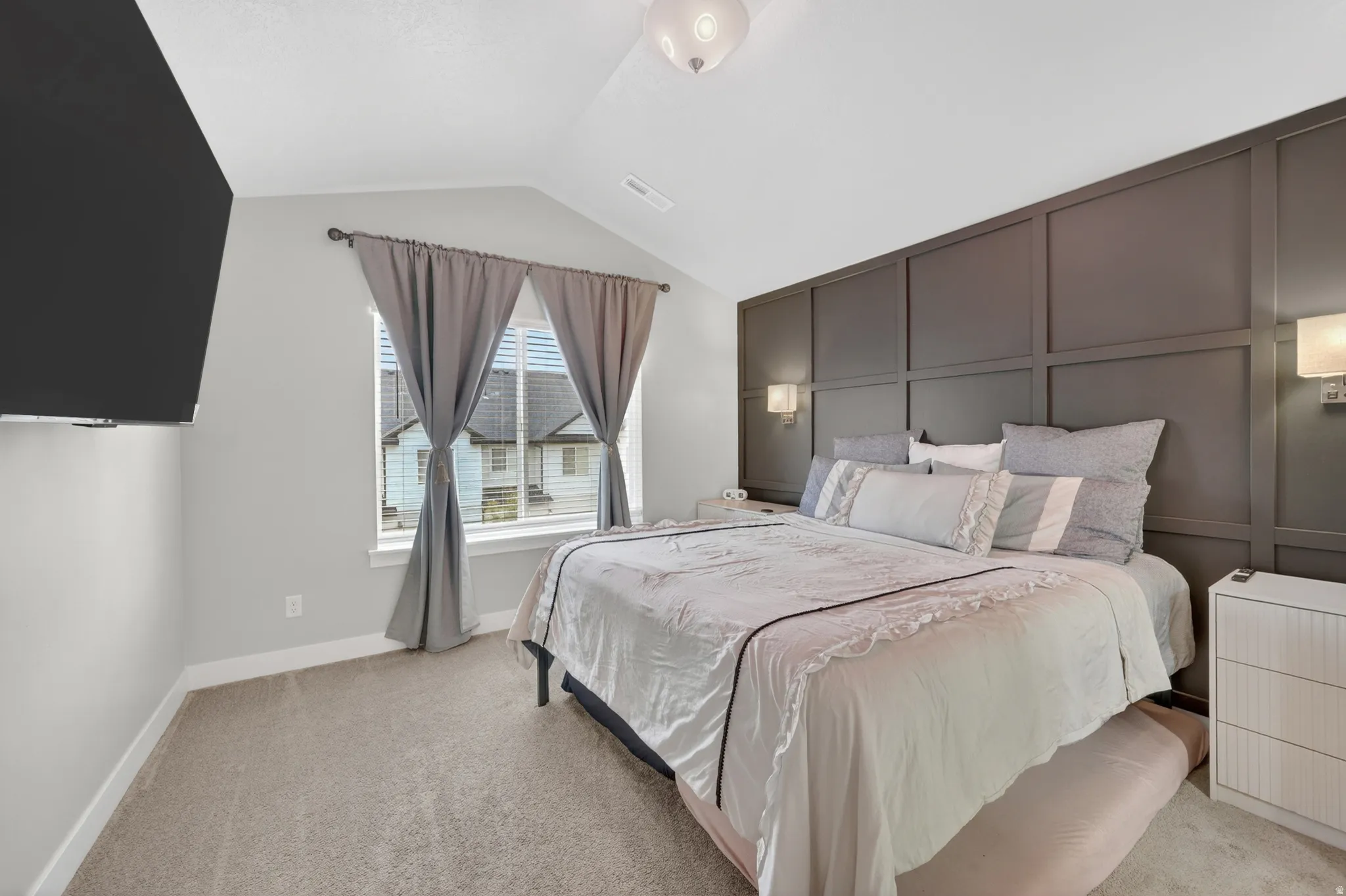 Bedroom featuring a decorative accent wall with sconce lighting, vaulted ceilings, and carpeted flooring