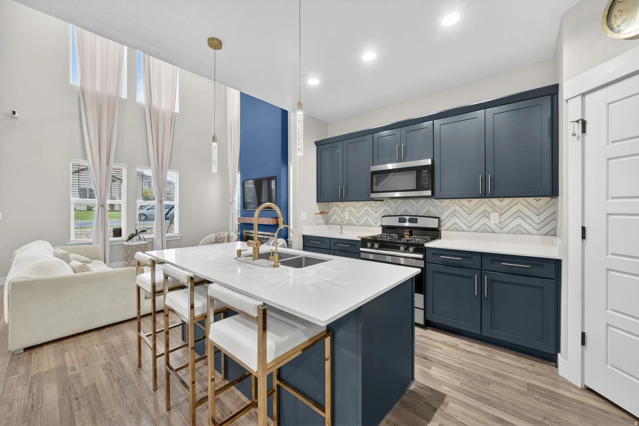 Open-concept kitchen featuring dark blue cabinetry, light wood-finish flooring, and a central island with white countertops