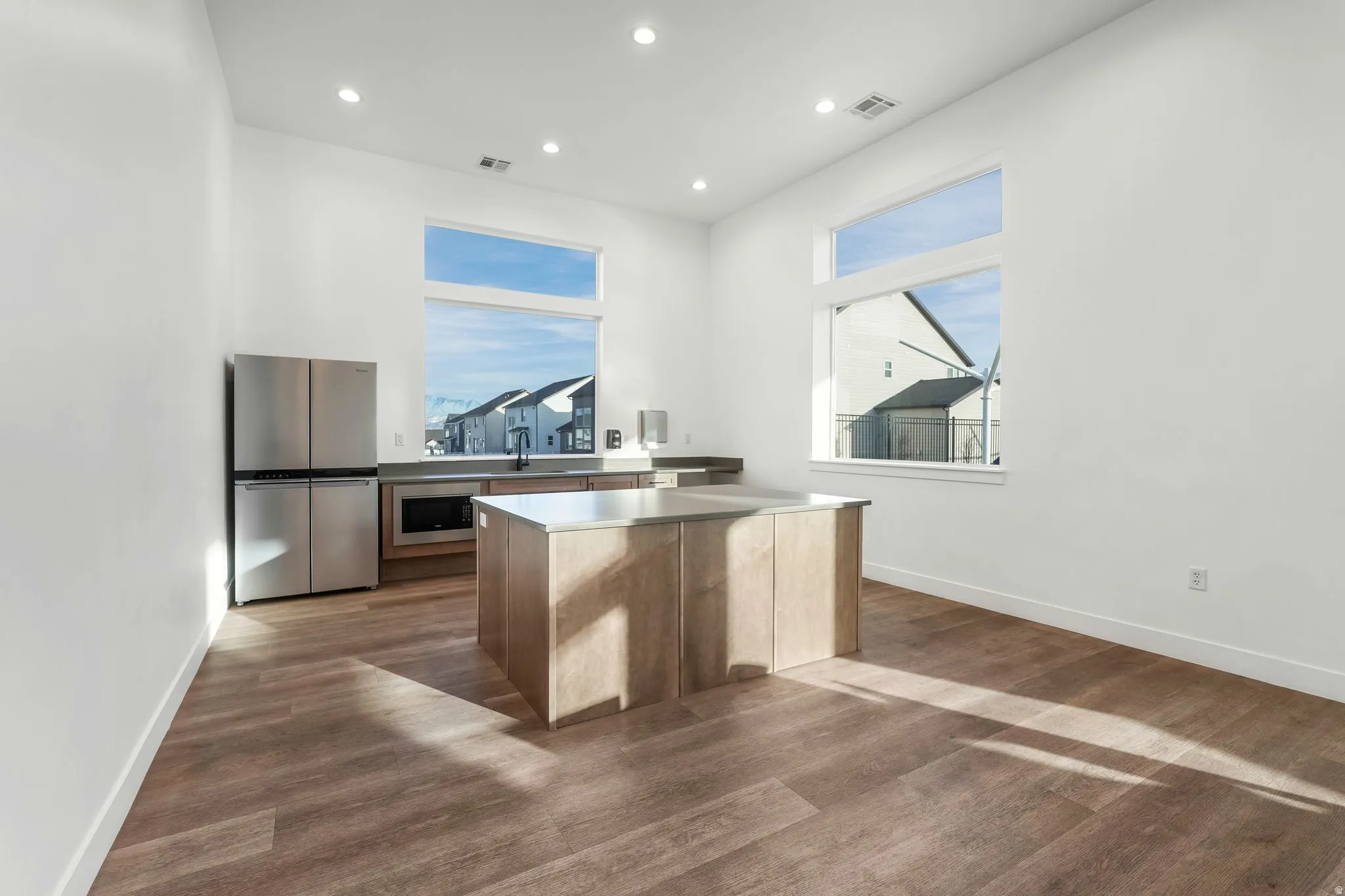 Open-concept room featuring wood-finish flooring, a central island with a solid surface countertop, and stainless steel appliances
