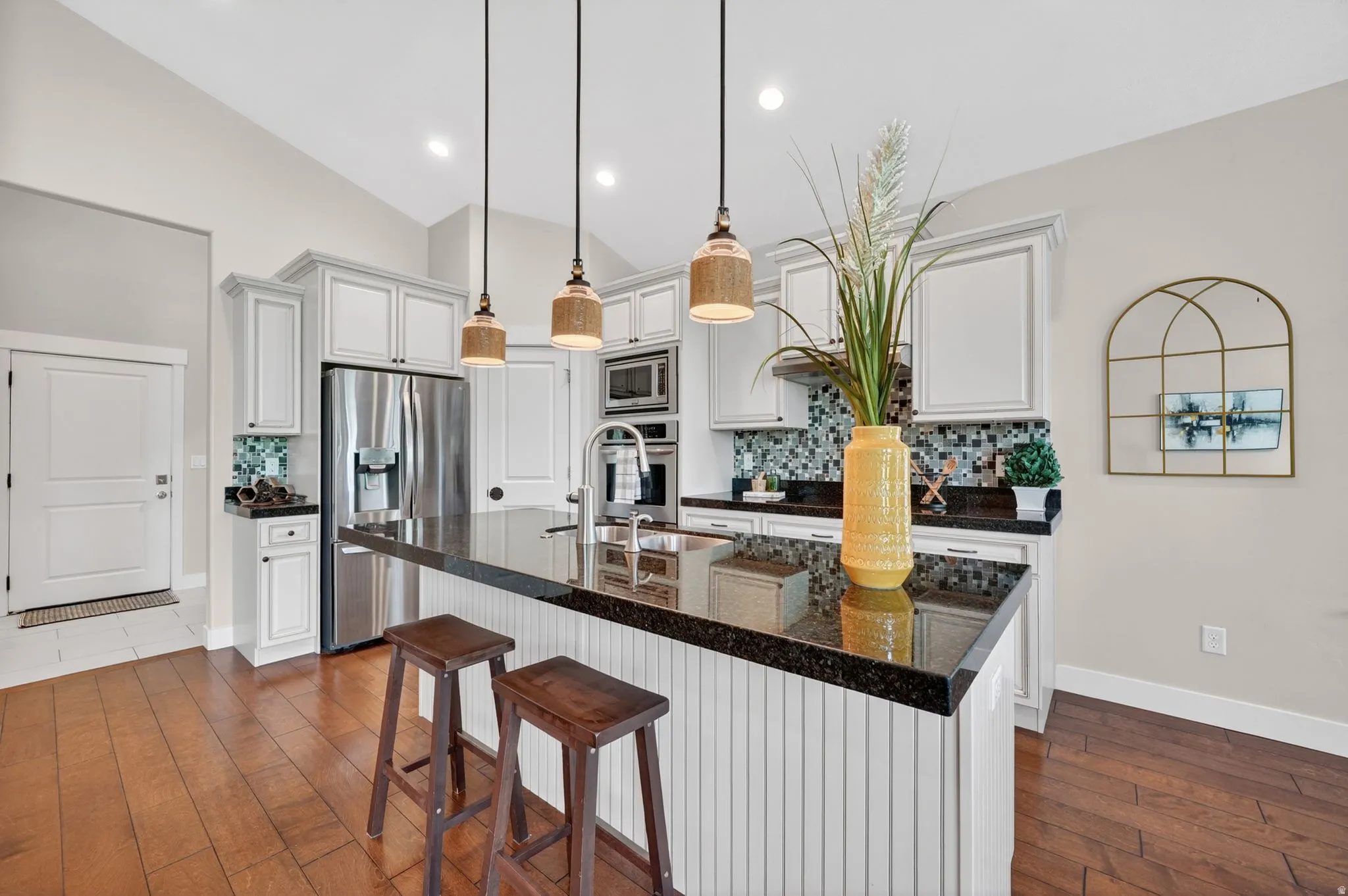 Kitchen featuring a large island with dark countertops and white beadboard paneling, stainless steel appliances, white cabinetry, and wood-finish flooring