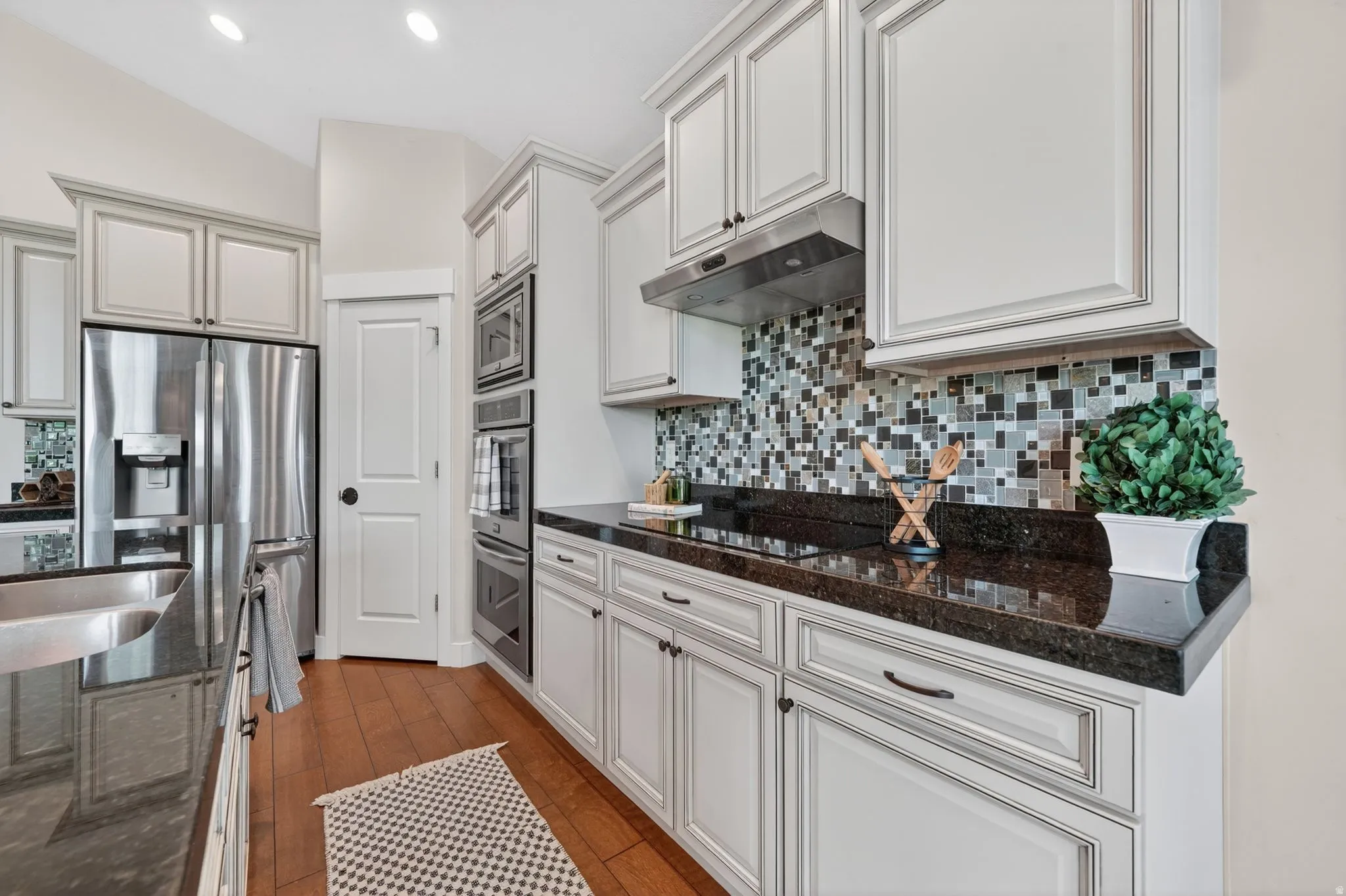Kitchen featuring white shaker-style cabinetry, dark stone countertops, and a multi-toned mosaic tile backsplash