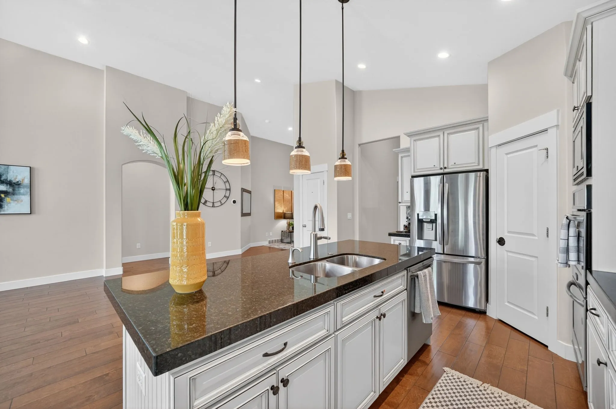 Kitchen island featuring a dark stone countertop, undermount stainless steel sink, and three pendant lights