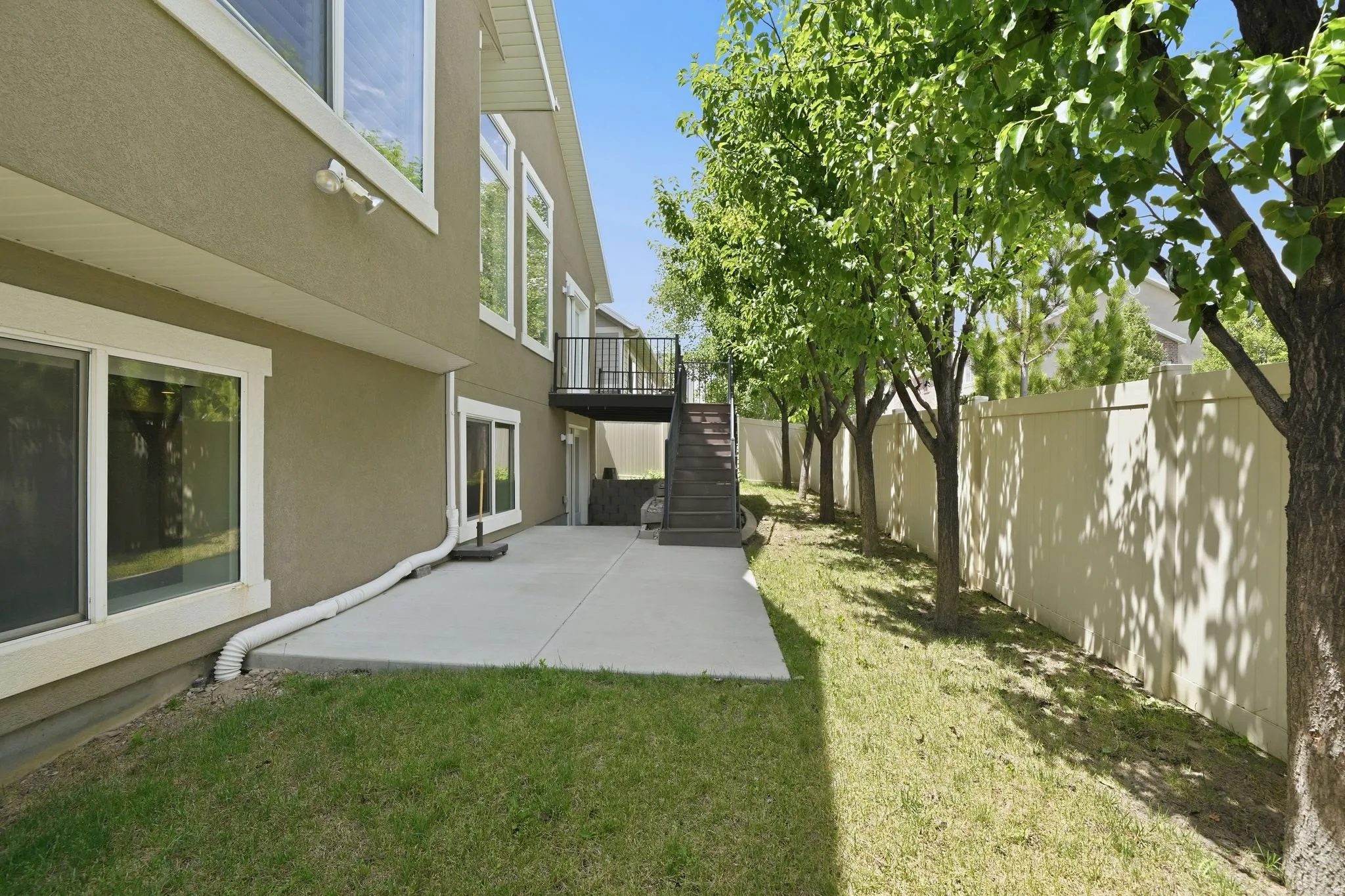 Rear exterior featuring a concrete patio, stucco siding, and a second-story balcony with stairs