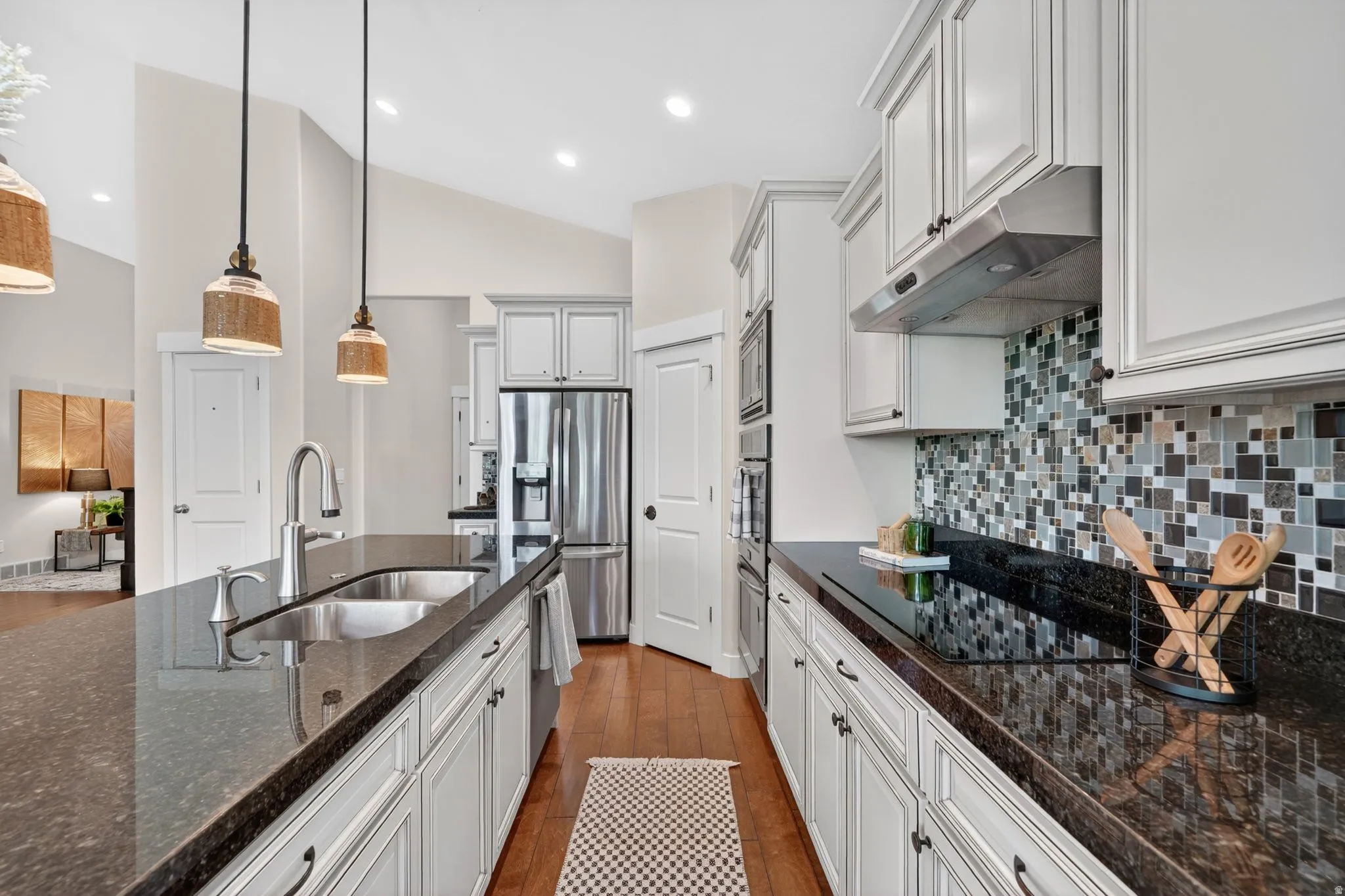 Kitchen featuring an island with undermount sink, granite countertops, white cabinetry, stainless steel appliances, and a mosaic tile backsplash