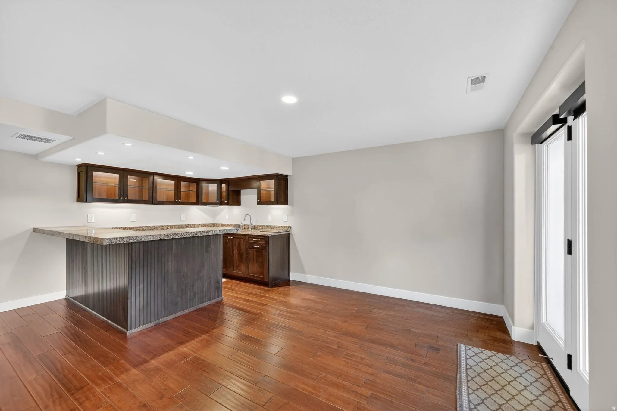 L-shaped wet bar featuring rich wood cabinetry, integrated sink, and stone-finish countertops