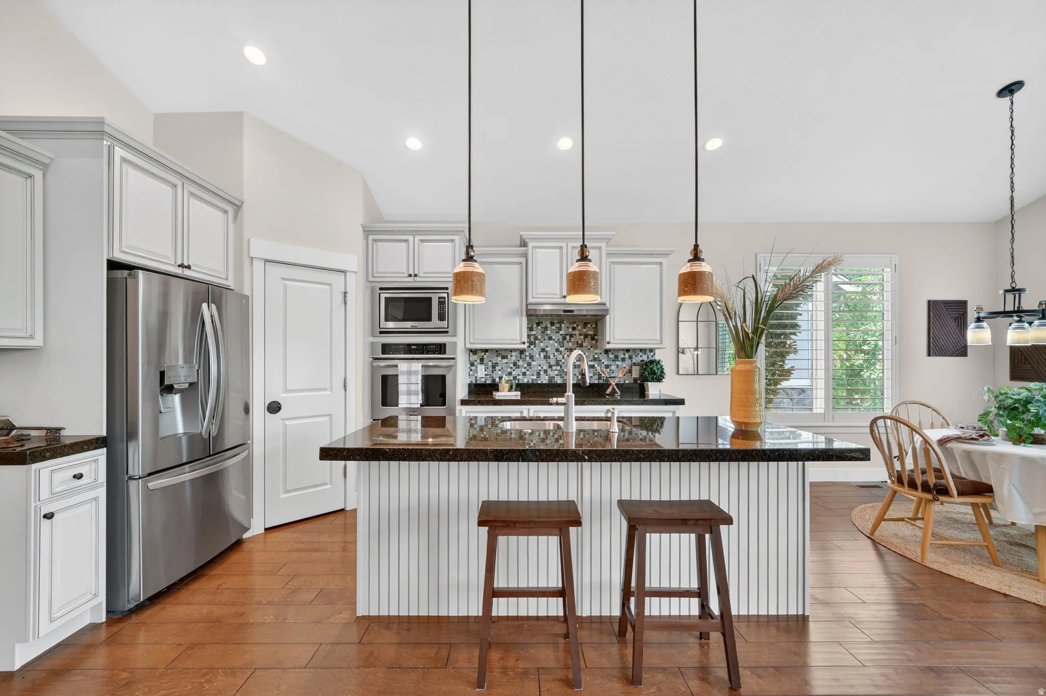 Gourmet kitchen featuring a central island with dark stone countertop, pendant lighting, white cabinetry, integrated stainless steel appliances, and wood-finish flooring