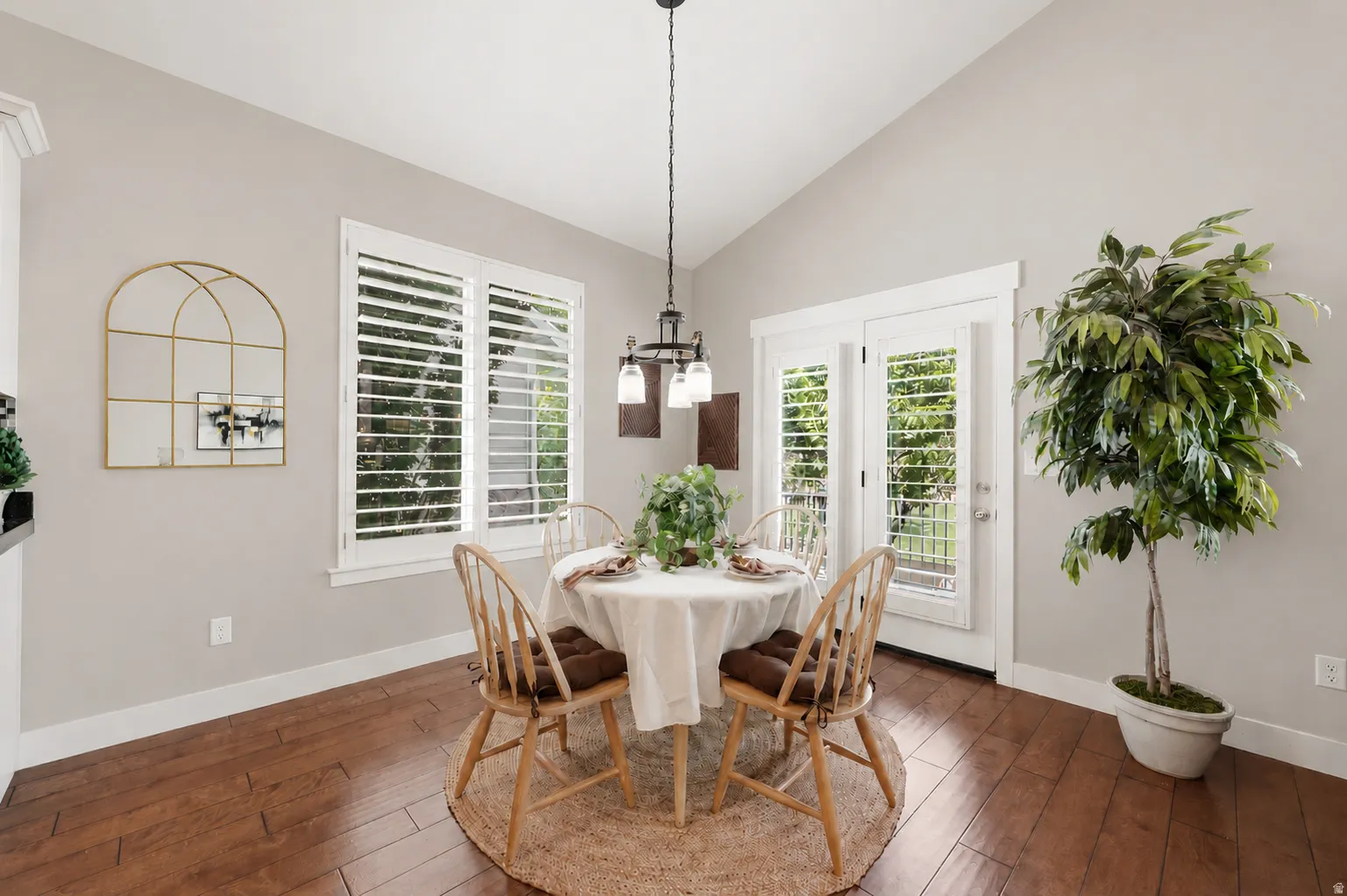 Dining area featuring wood-finish flooring, vaulted ceiling, and white plantation shutters on windows and French doors