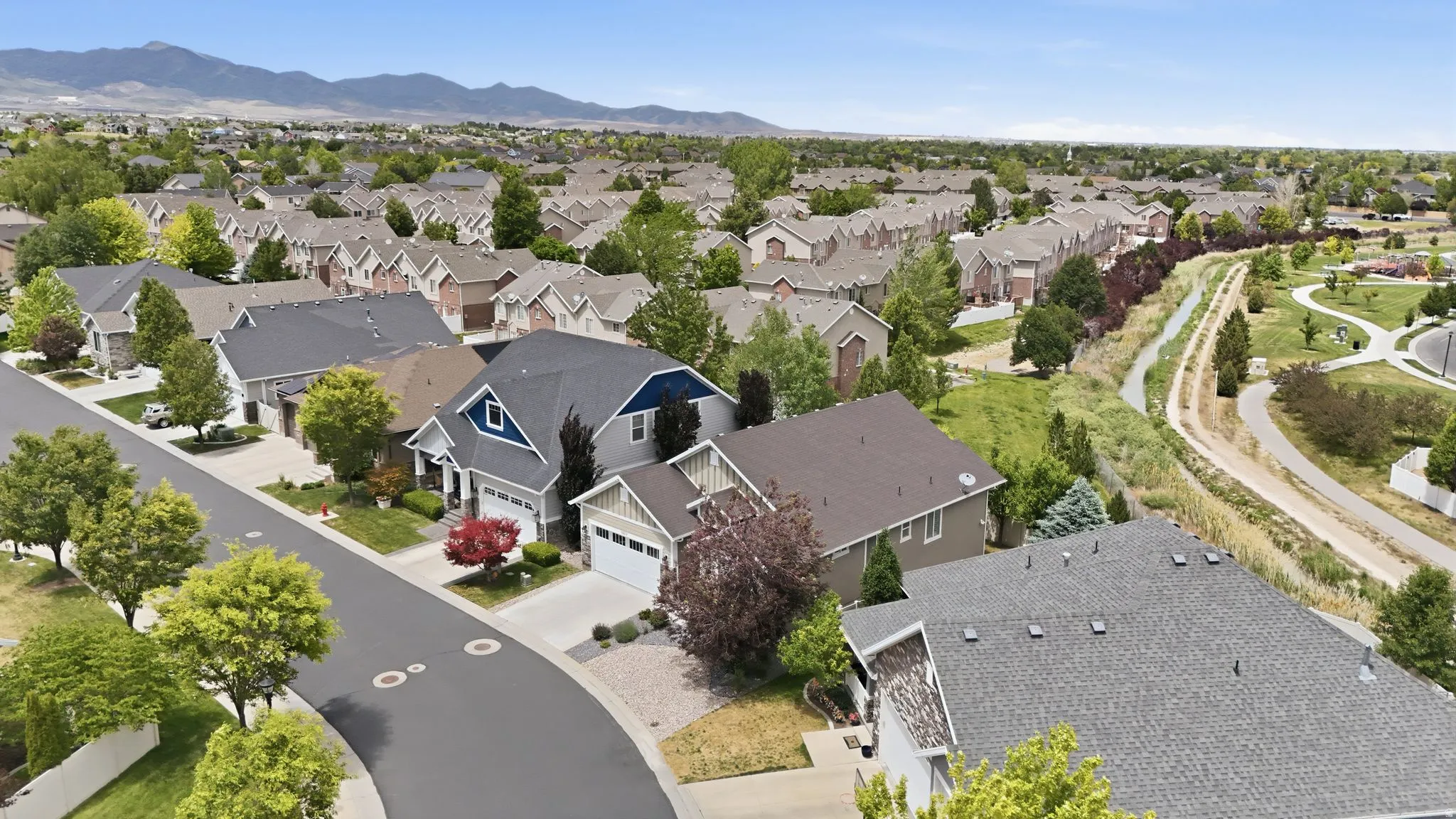 Residential neighborhood featuring single-family homes and townhomes, a paved street, mature trees, and a greenbelt with walking paths