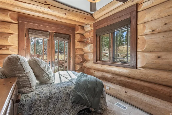 Log-style interior featuring natural wood walls, a ceiling fan, and two windows with wood blinds