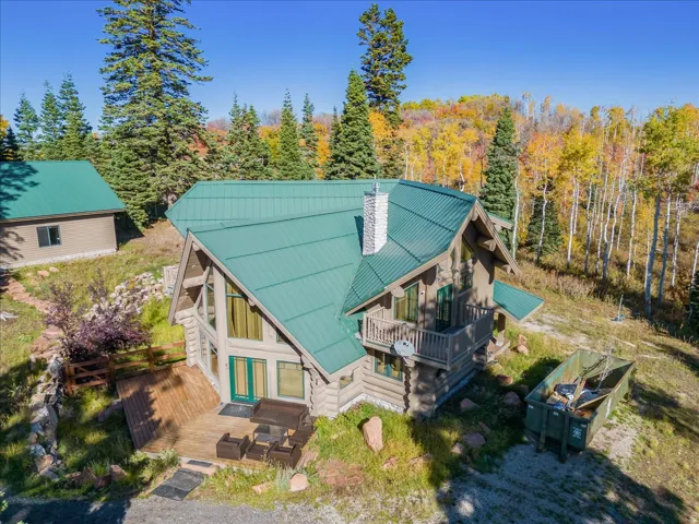 Log-sided home featuring a green metal roof and a prominent stone chimney