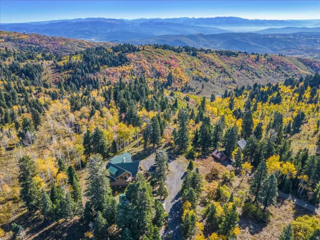Expansive mountainous landscape featuring a single-family residence with a green roof, surrounded by mature evergreen trees and deciduous trees with autumn foliage
