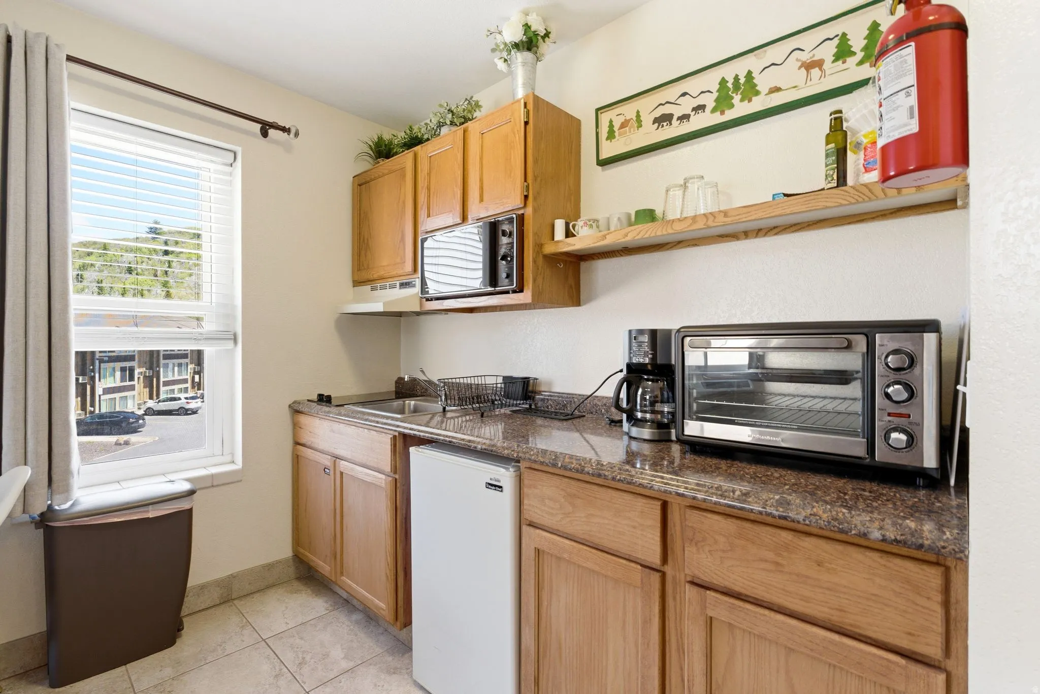 Compact kitchen space featuring light wood cabinetry, a built-in microwave, and a stainless steel sink