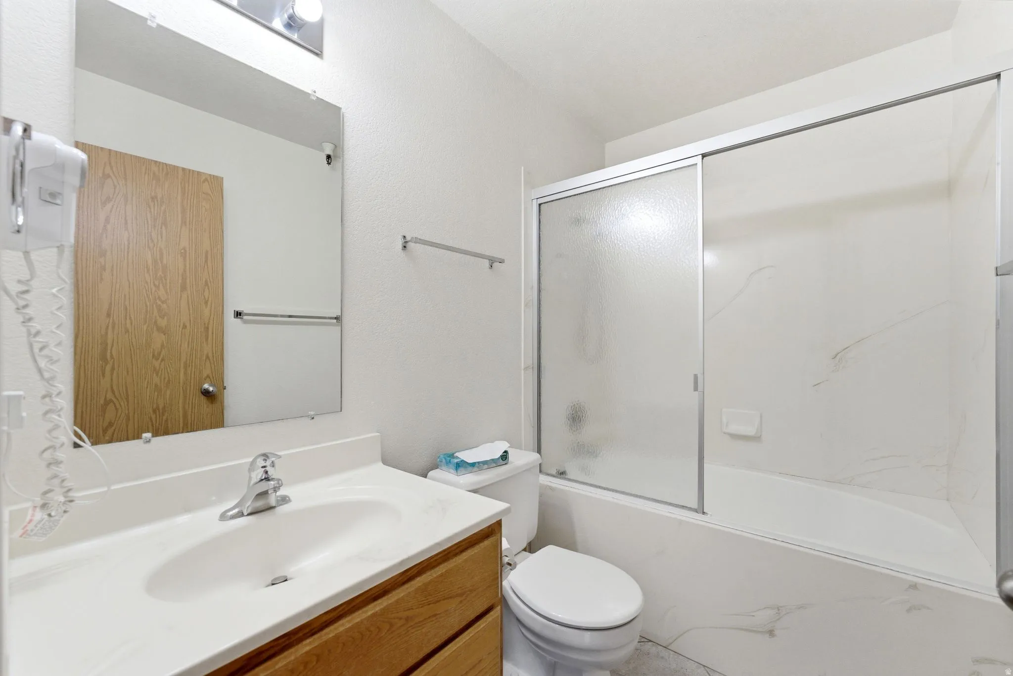 Bathroom featuring a wood-finish vanity with an integrated white sink, a chrome faucet, and a sliding glass shower door