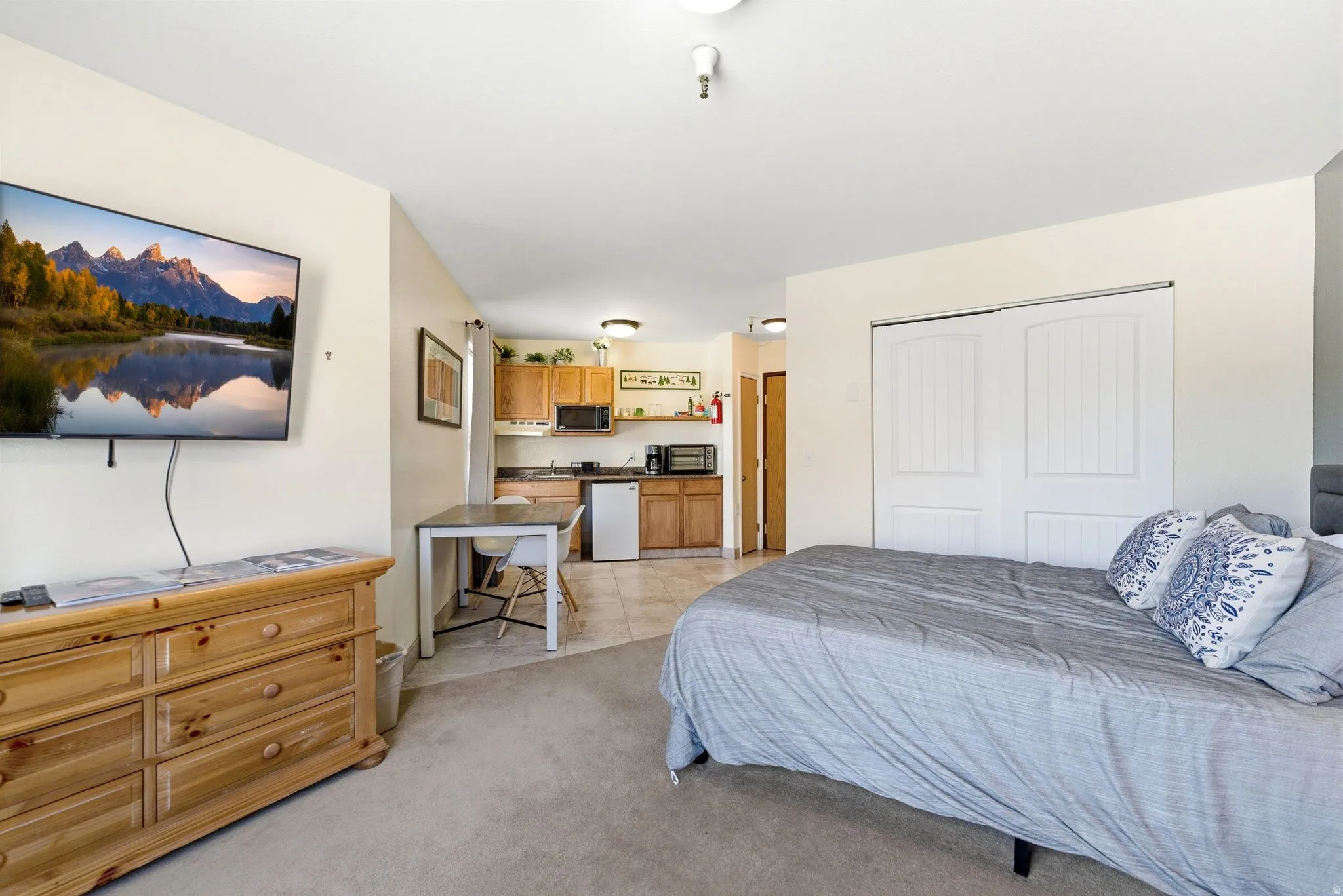 Open-concept studio space featuring carpeted flooring, a kitchen area with wood-finish cabinetry, and a full-size refrigerator