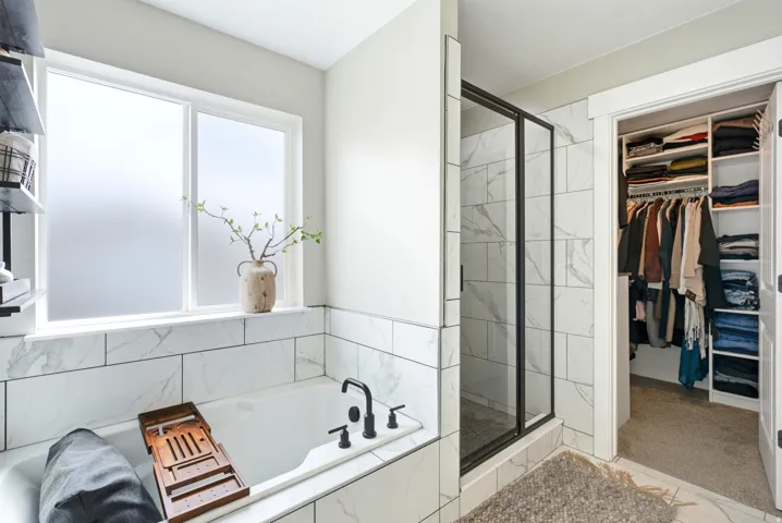 Soaking tub with black fixtures, tiled surround, and privacy window
