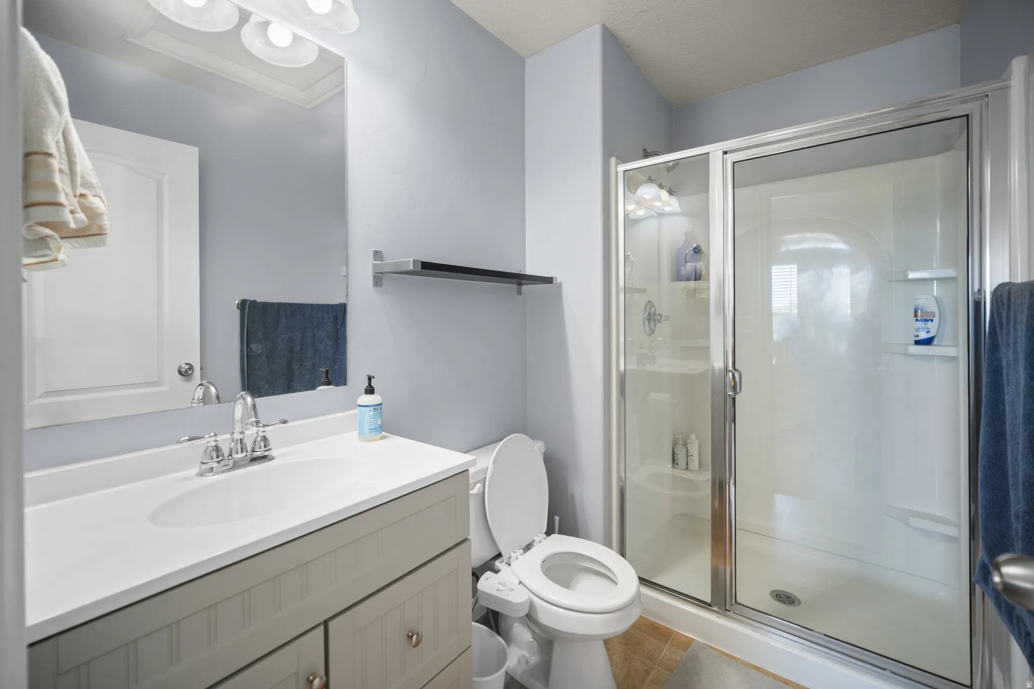 Bathroom featuring a glass-enclosed shower, single vanity with integrated sink, chrome faucet, and tiled flooring