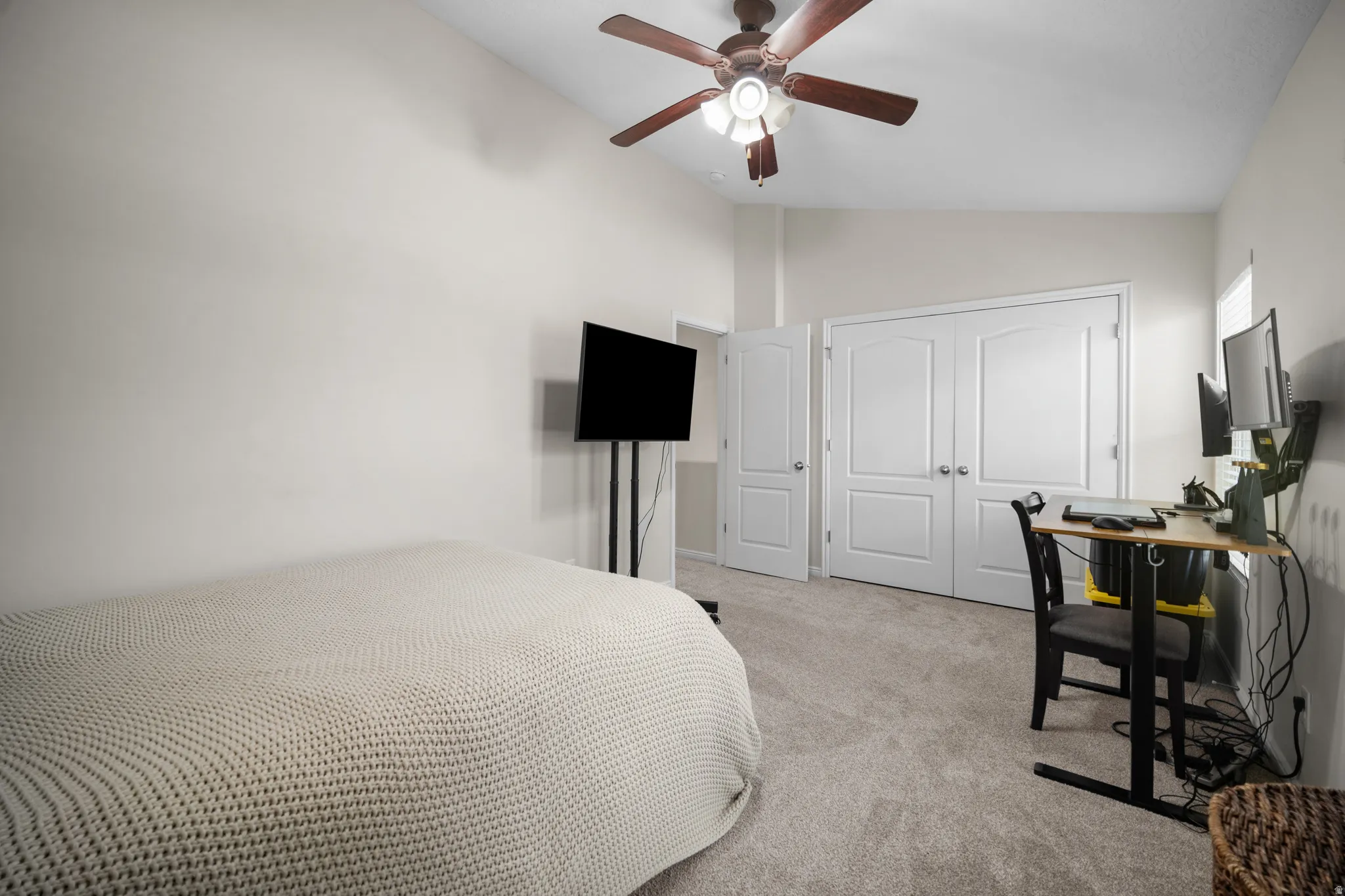 Spacious room featuring vaulted ceilings, a ceiling fan with integrated lighting, light gray carpeting, and white double-door closet