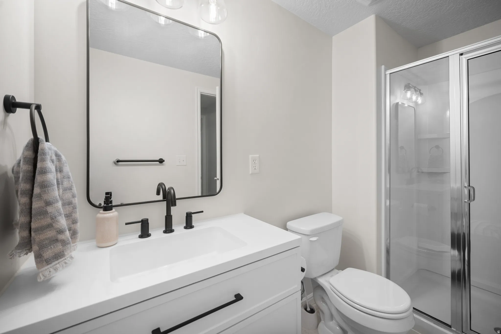 Bathroom featuring a white vanity with integrated sink, black fixtures, framed mirror, and a glass-enclosed shower