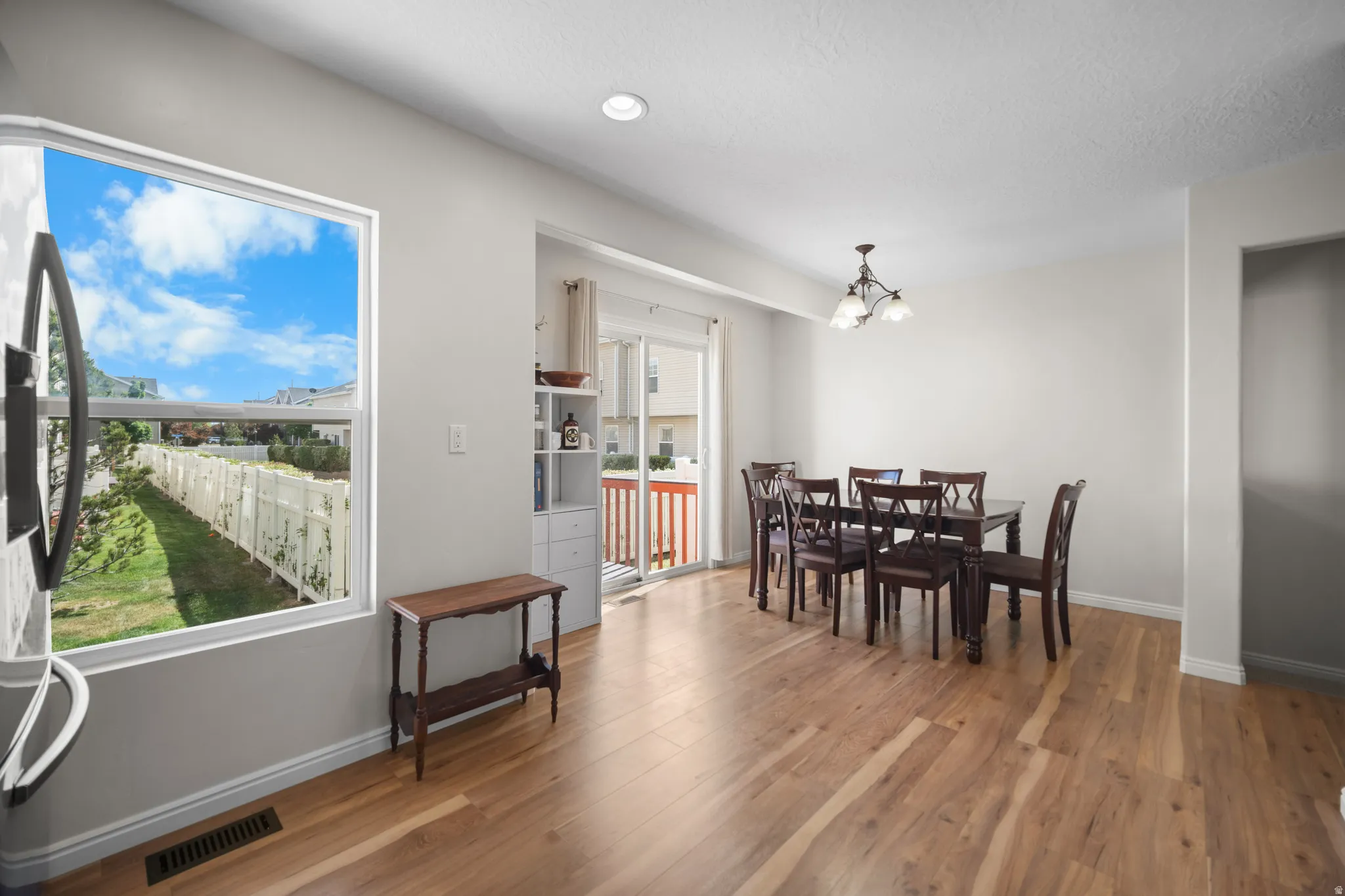 Expansive room featuring wood-finish flooring, a contemporary ceiling light fixture, recessed lighting, and a large window overlooking a fenced yard