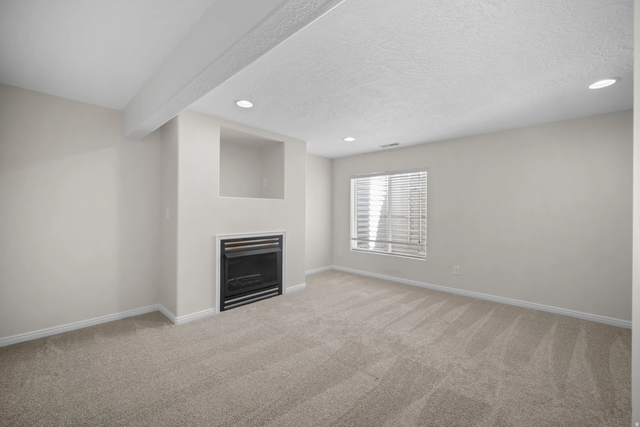 Carpeted room featuring a built-in fireplace with a black metal insert and a recessed alcove