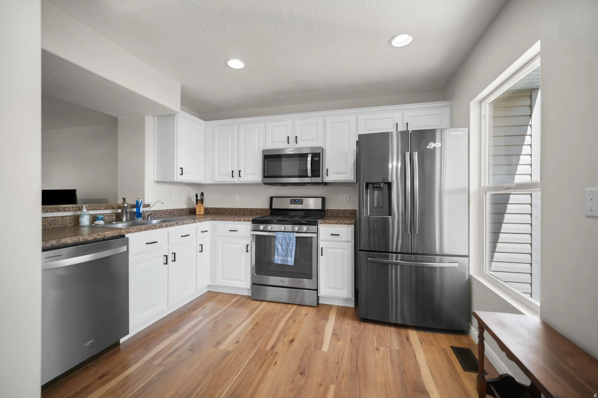 Kitchen featuring wood-finish flooring, white cabinetry with dark hardware, stainless steel appliances, recessed lighting, and a window