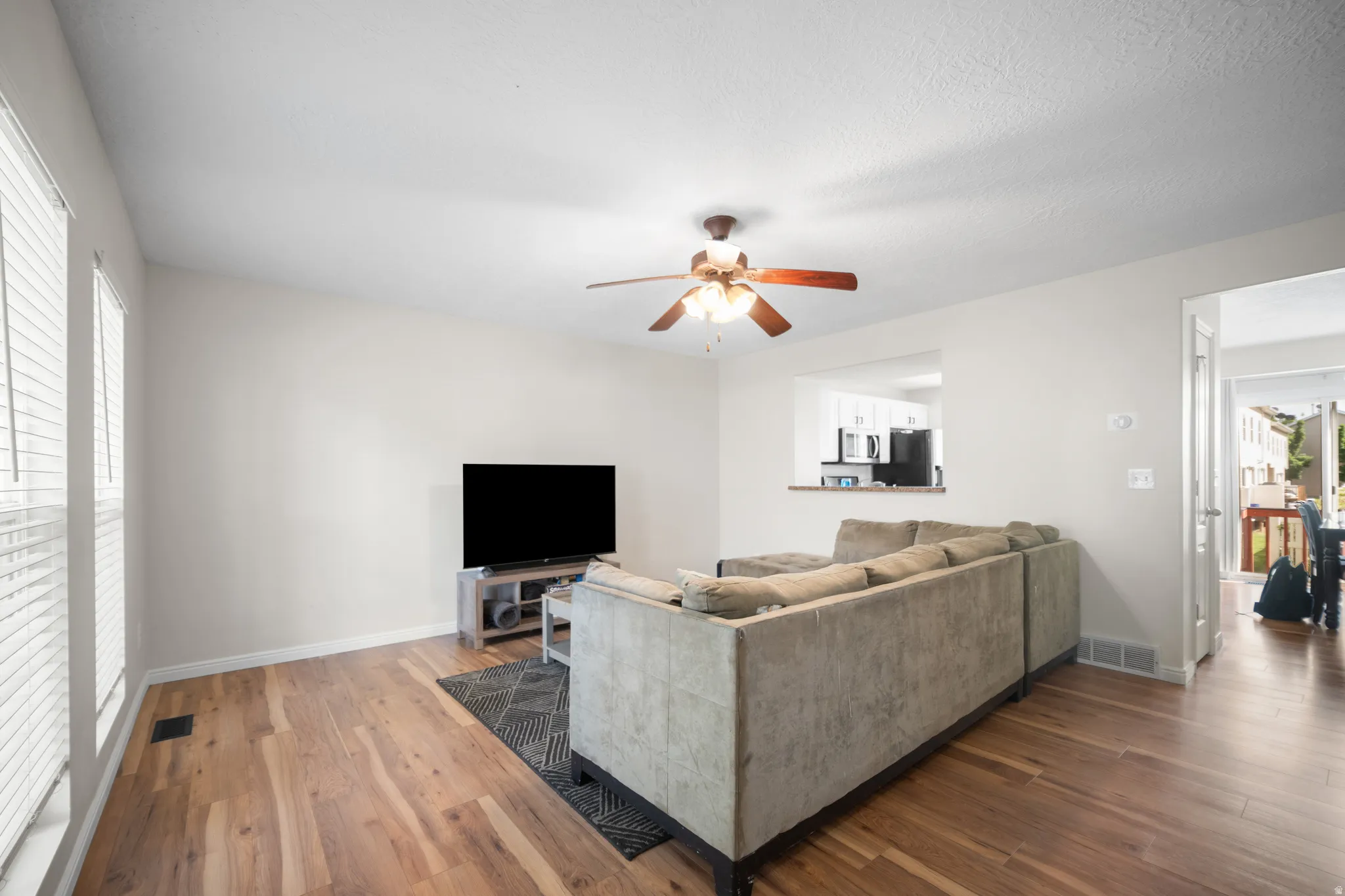Spacious living area featuring wood-finish flooring, ample natural light from multiple windows, and a ceiling fan