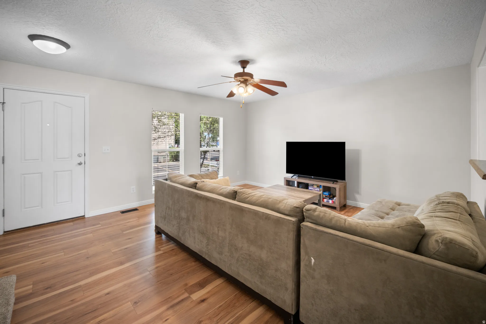 Open living area featuring wood-finish flooring, light grey walls, and a ceiling fan with light fixture