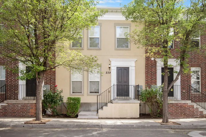 Multistory townhome facade featuring a cream stucco finish and brick accents