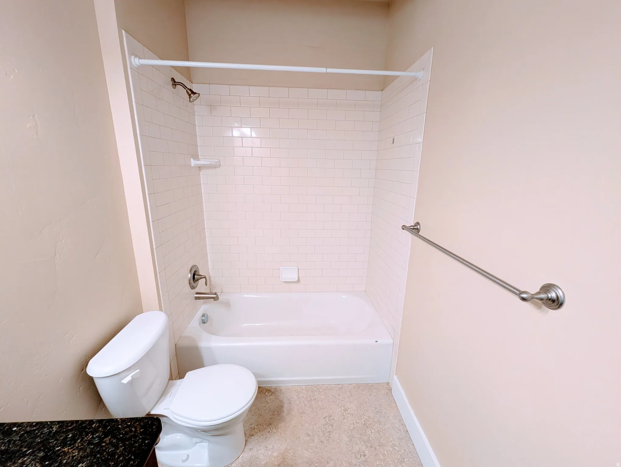 Bathroom featuring a white subway tile surround bathtub with a brushed nickel showerhead and faucet, a white toilet, and a dark stone-finish countertop