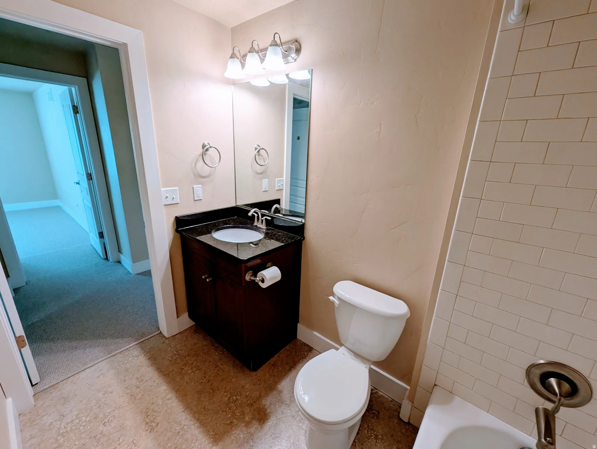 Bathroom featuring a dark wood vanity with a stone countertop, a rectangular mirror, a three-light fixture, and a white toilet