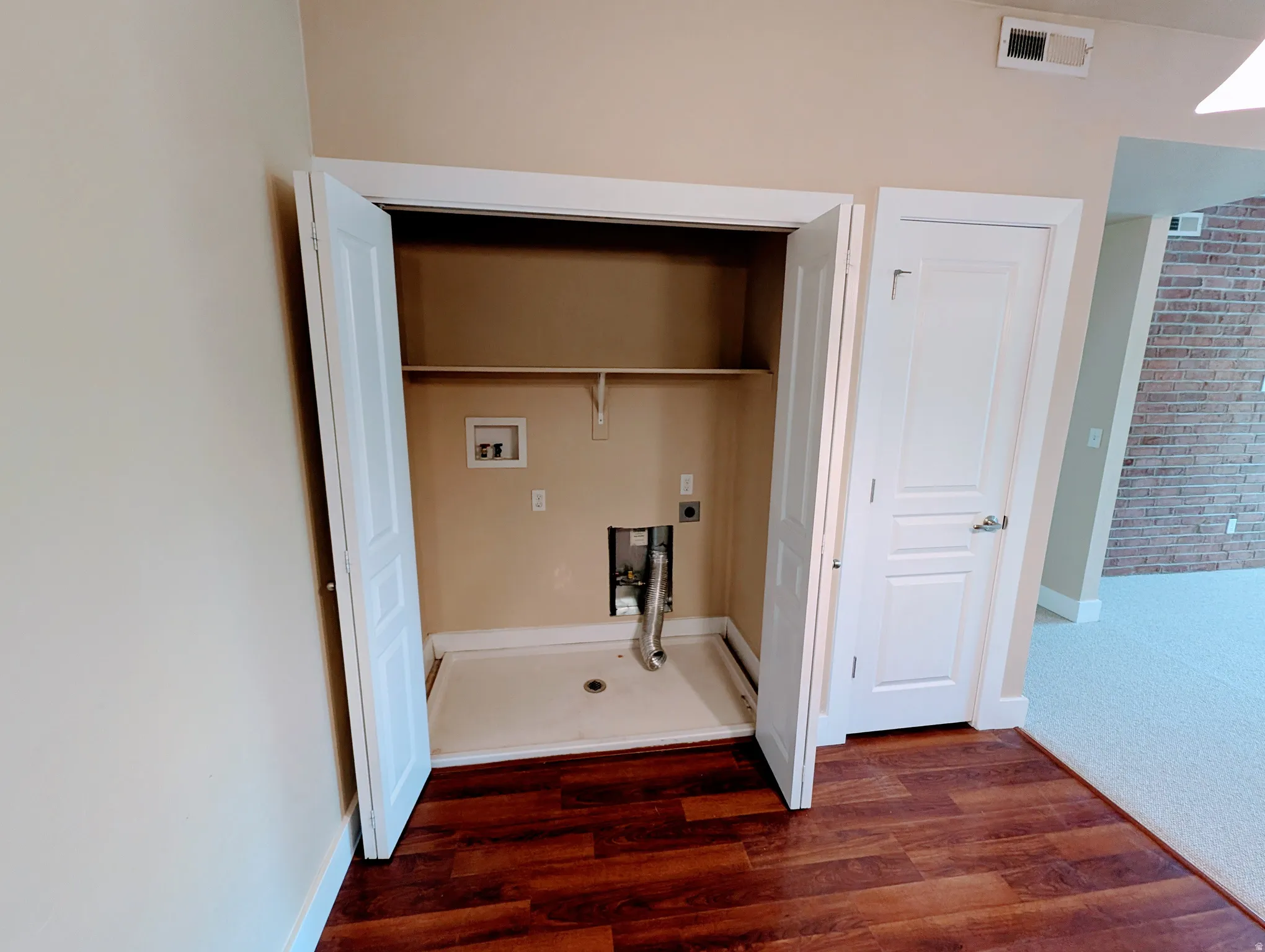 Dedicated laundry closet featuring a utility shelf, hookups, and a drain pan, complemented by rich wood-finish flooring and neutral wall tones