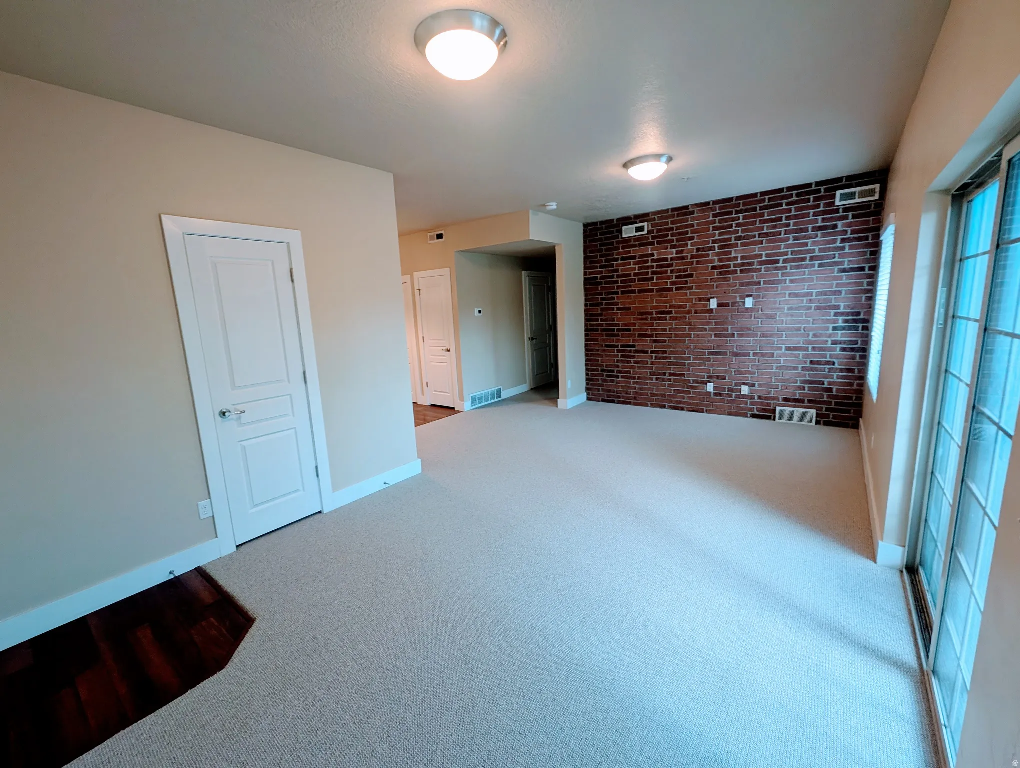 Spacious interior featuring a brick-accent wall, light-toned carpeting, and a sliding glass door